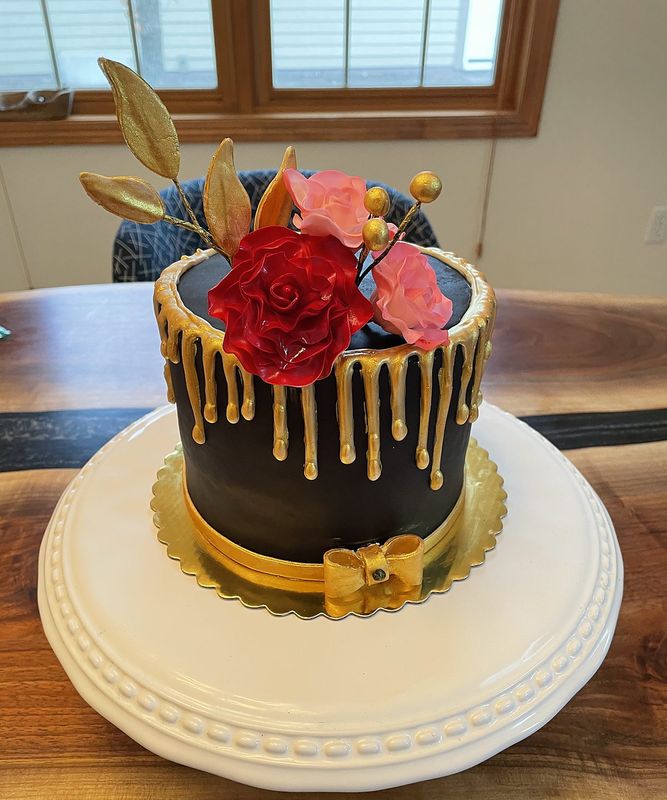 Black drip cake with gold drips, red roses and gold leaves
