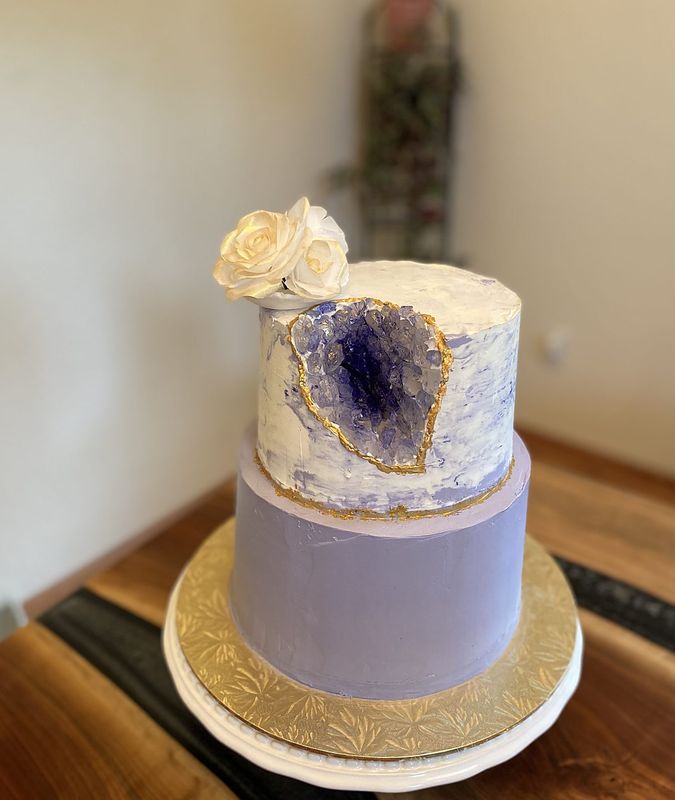 Two-tier lavender cake with a sparkling amethyst geode and white sugar rose