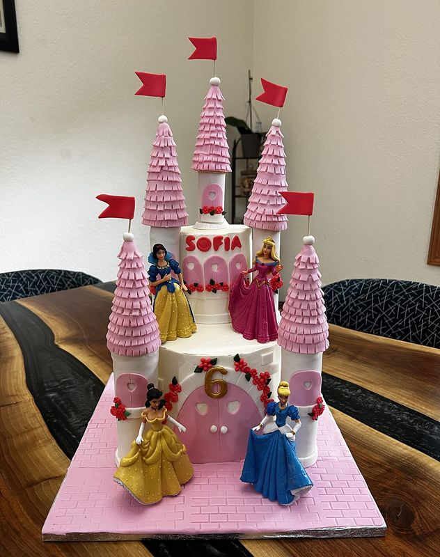 Pink princess castle cake with turrets, flags and princess figurines